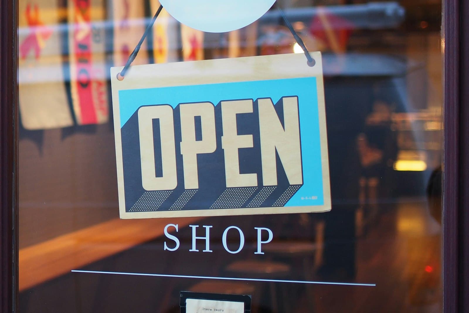 An OPEN sign hanging in a shop window, with the word SHOP printed on the glass. Regulars still need a path they recognize after the surface of a brand changes.