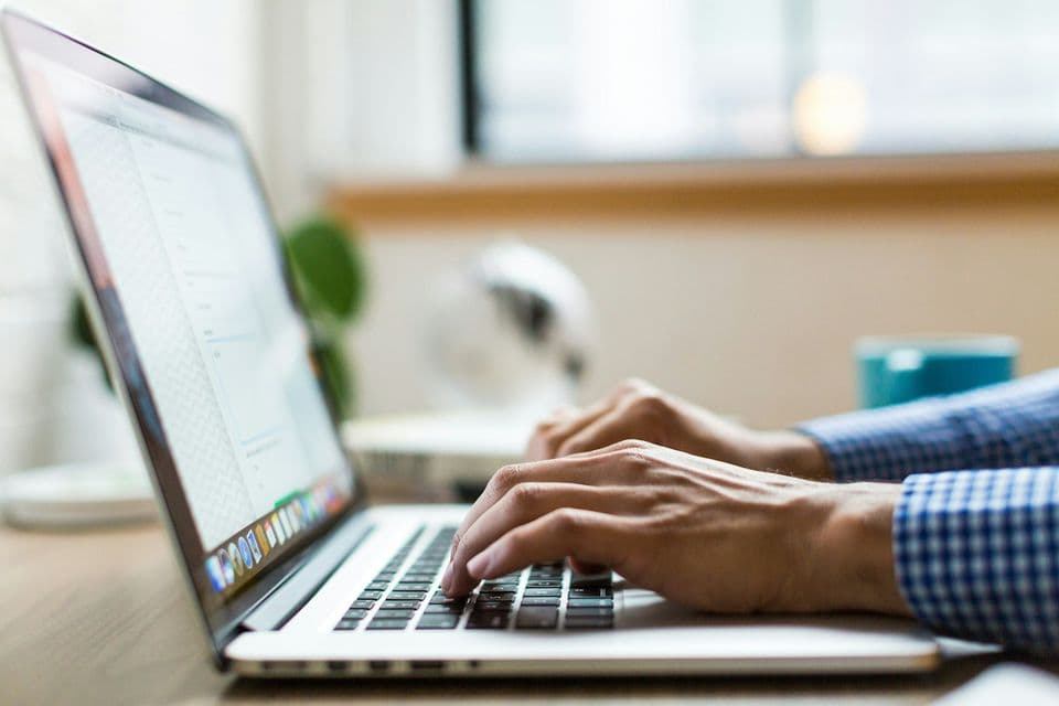 Hands typing on a laptop at a wooden desk near a window. The desk is where you time the old chore and the new review.