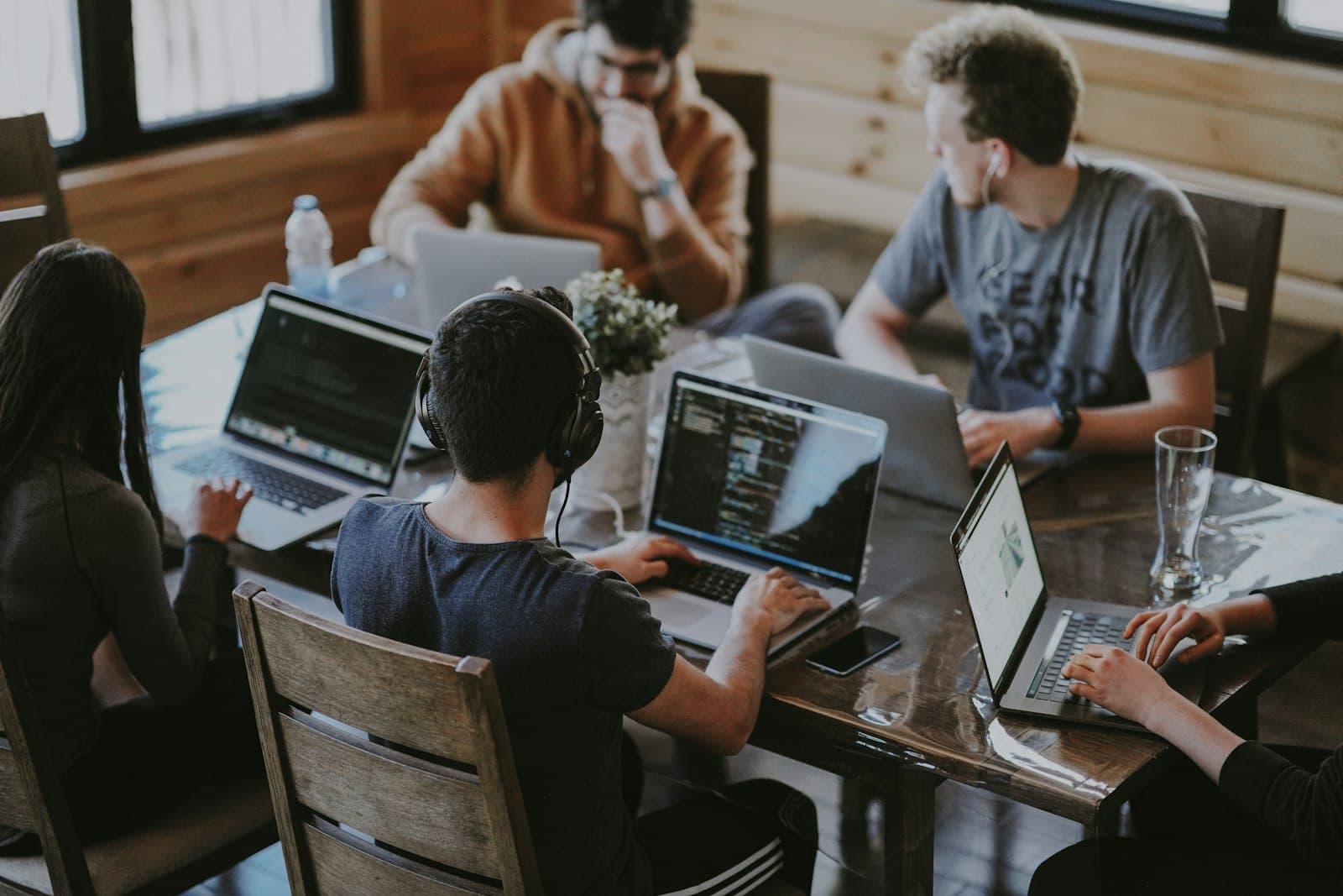 Five people working on laptops around a wooden table. A small group is a different seat from one specialist or a full-time hire.