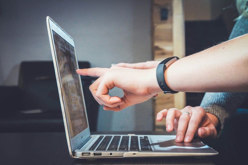 Two people pointing at a laptop screen, one wearing a fitness band. They are already in the work, which is the moment good onboarding tries to reach quickly.