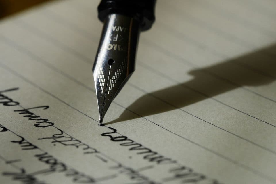 A close view of a fountain pen writing on lined paper, the slow choice of a title the page will have to keep.